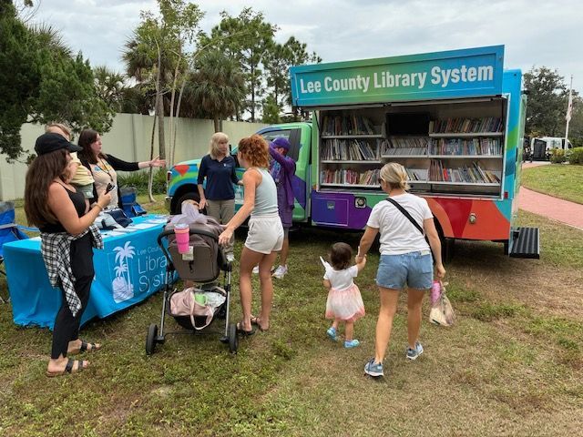 Mobile library with people, sunny day, offering books. People browsing, walking with a child.
