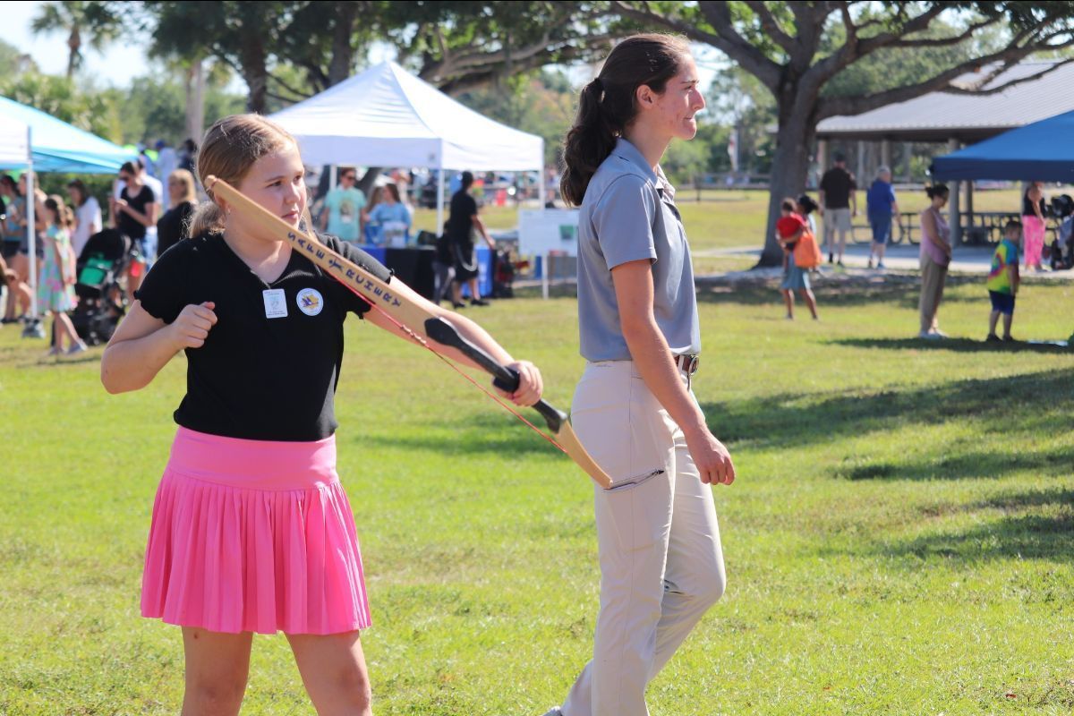 A girl in a pink skirt is holding a bat while walking with a woman in a blue shirt.