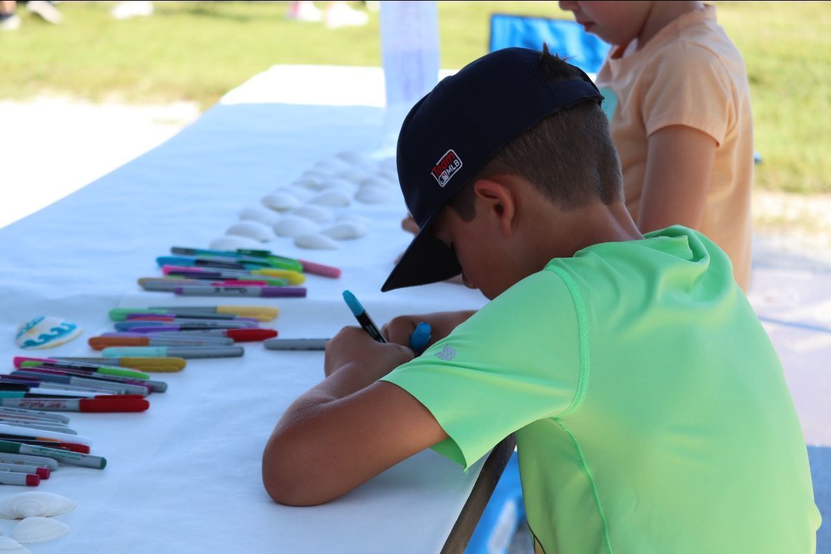 A boy in a green shirt is sitting at a table with markers