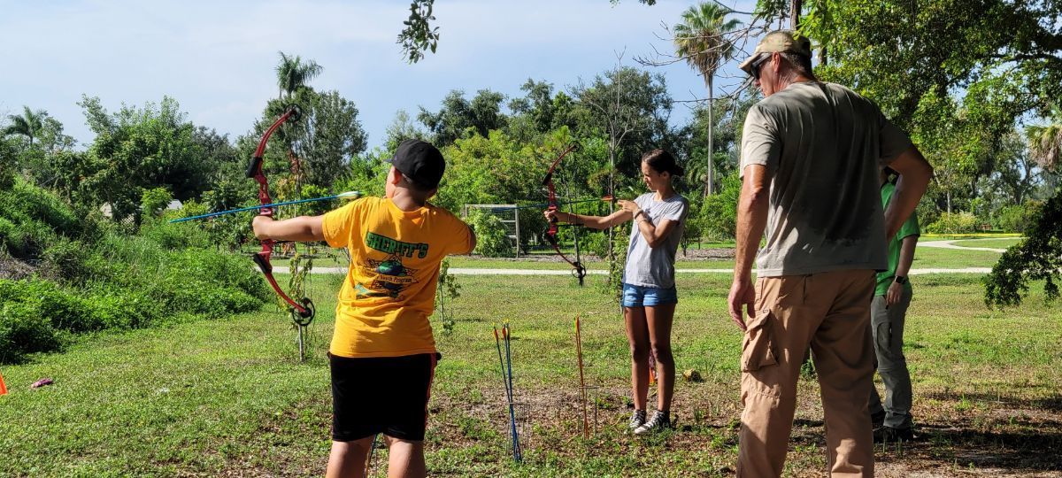 A group of people are playing archery in a park.