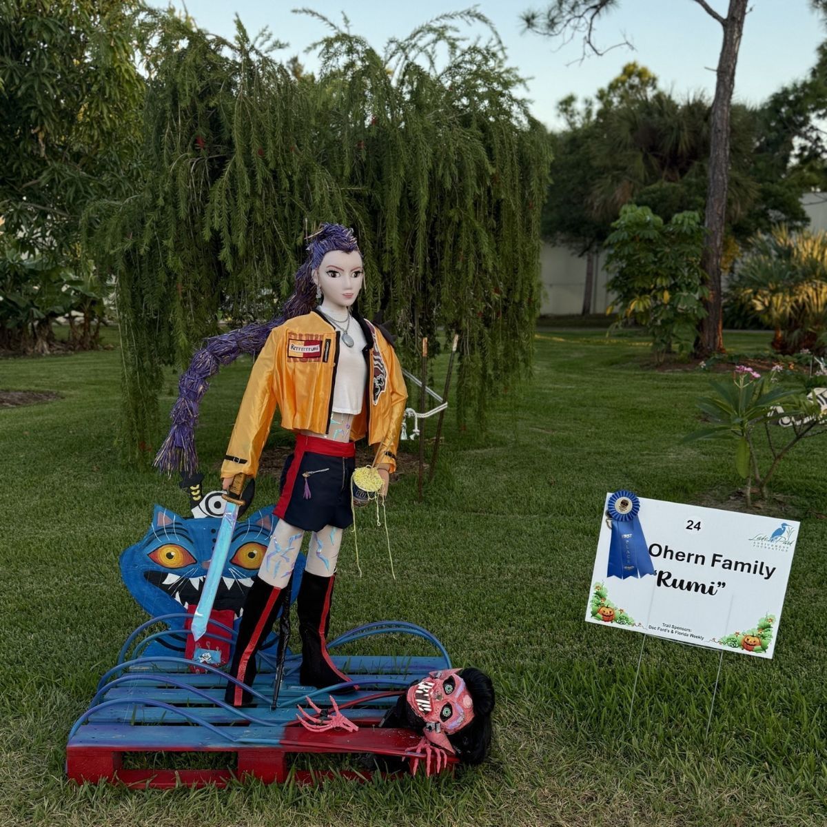 A sculpture of a character with a sword standing on a blue monster, with a detached head and a yellow jacket.