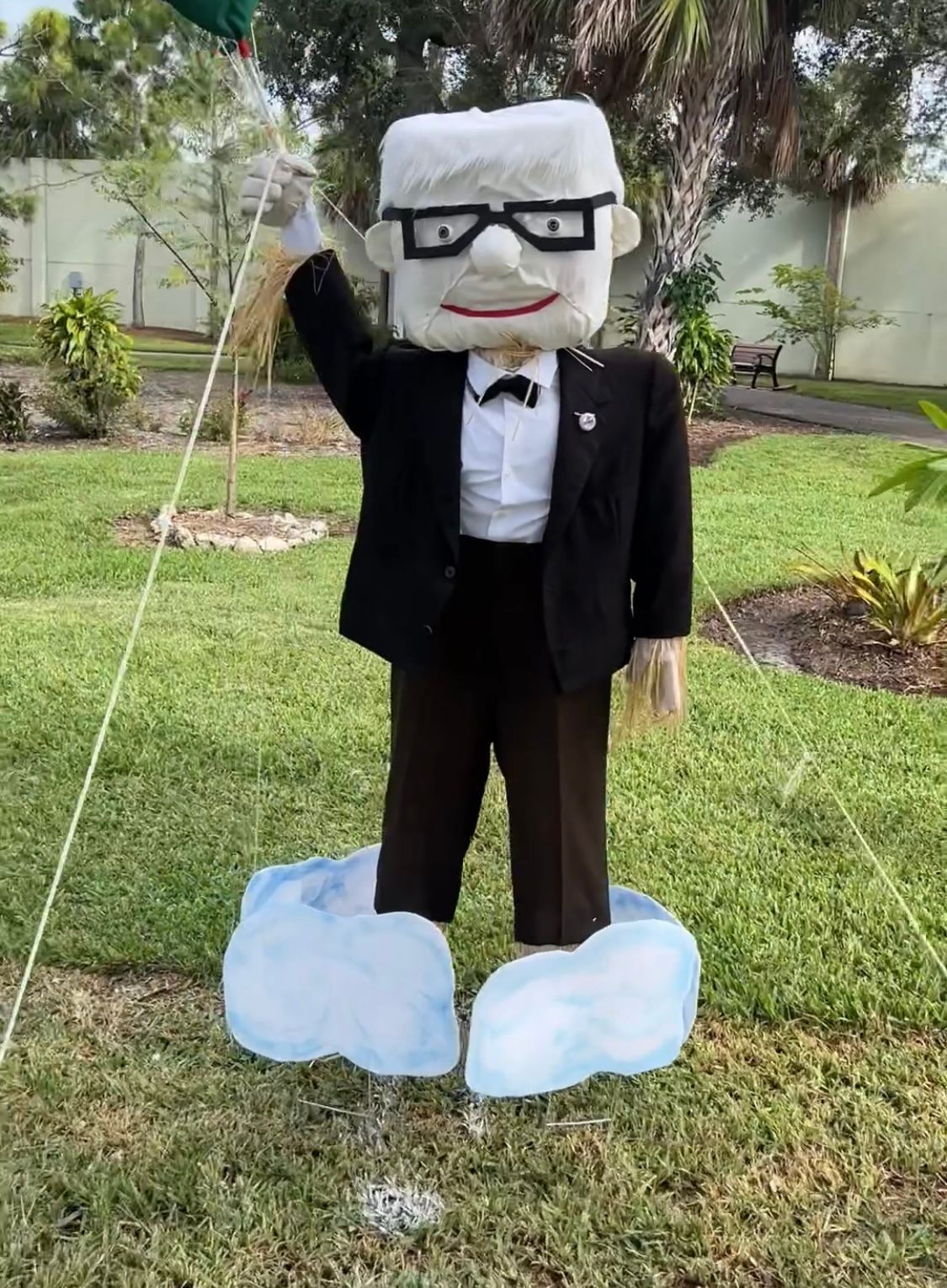 A scarecrow in a suit and bow tie is standing in the grass.