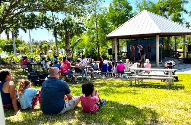 A group of people are sitting in the grass watching a performance in a park.