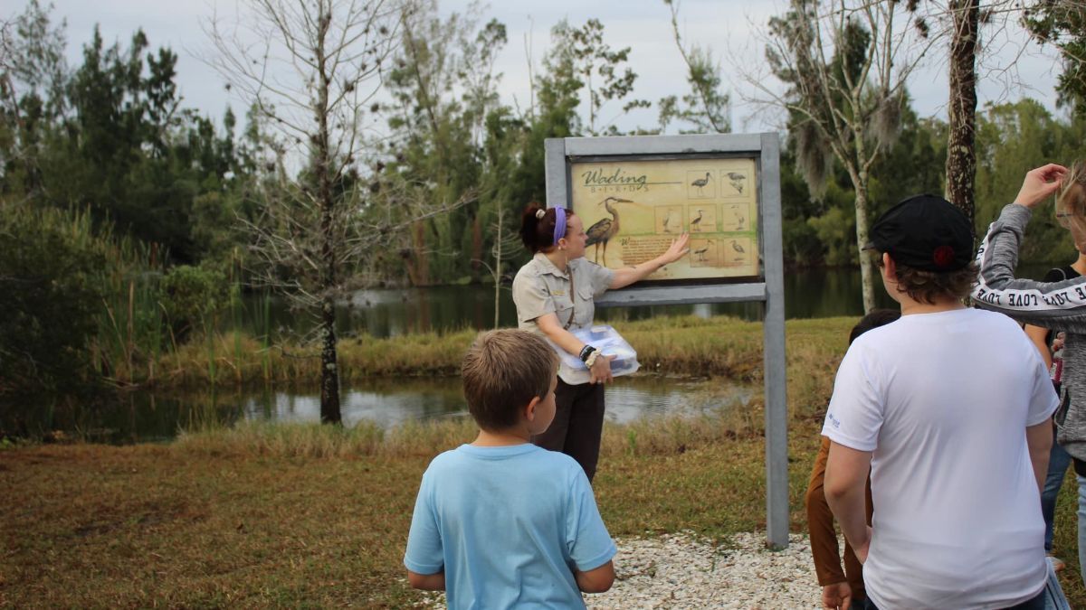 A group of people are standing in a field looking at a sign.