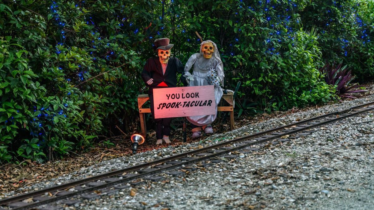 A couple of skeletons sitting on a bench next to a train track.