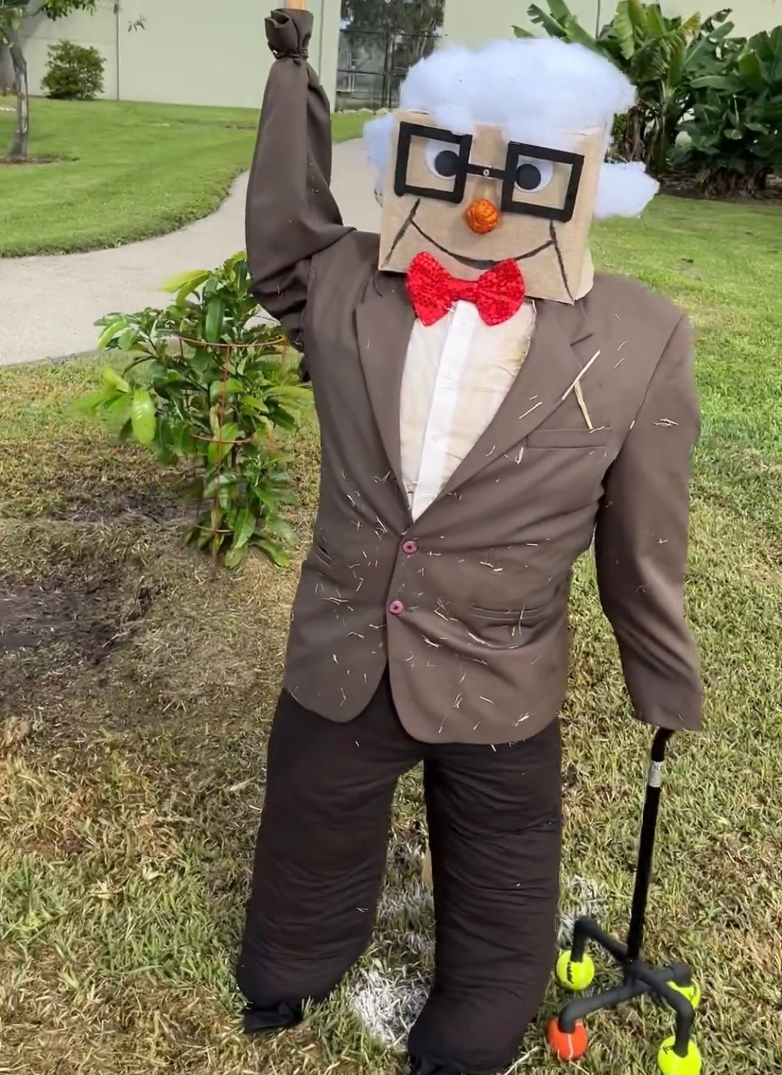 A scarecrow in a suit and bow tie is standing in the grass