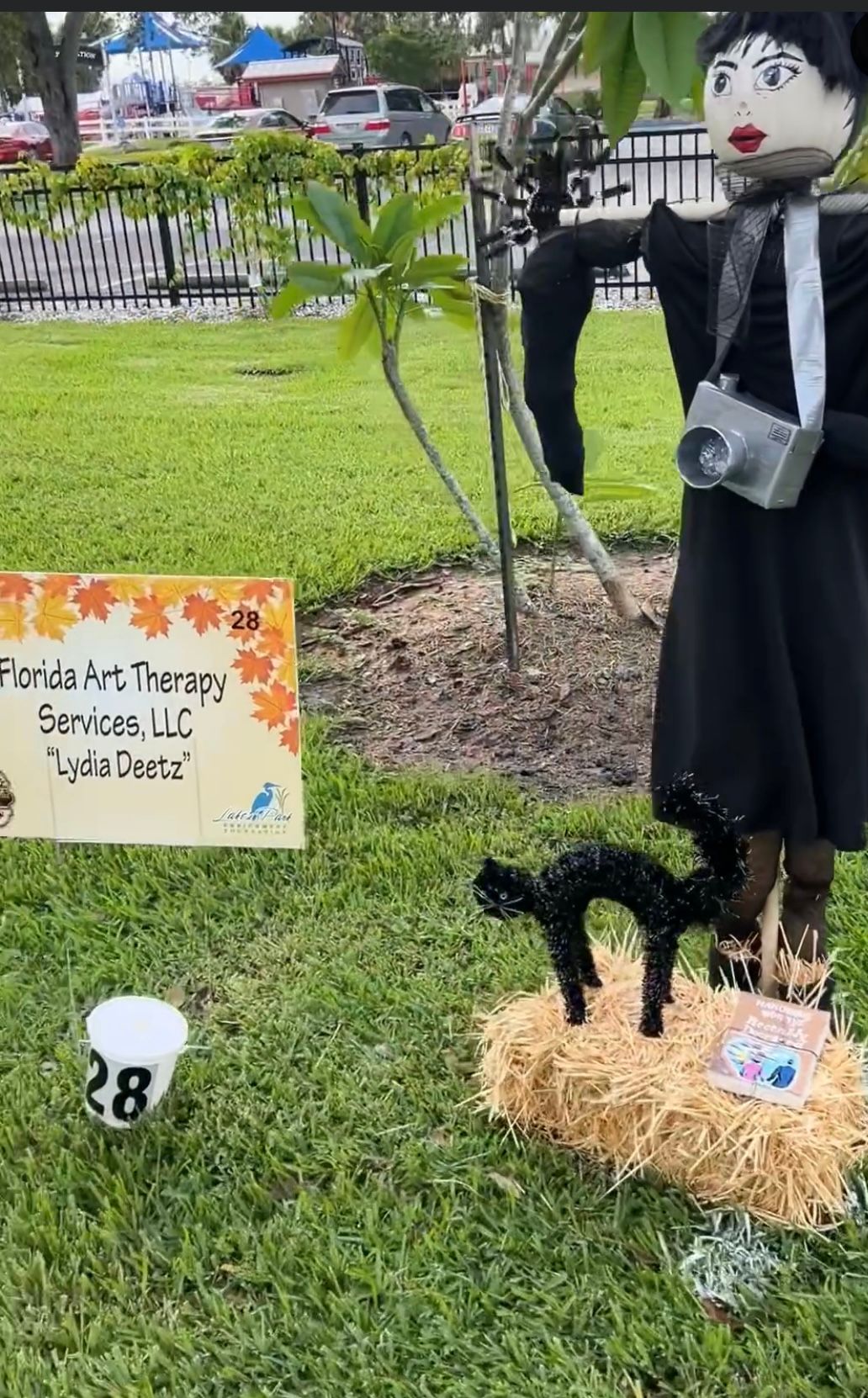 A scarecrow is standing in the grass next to a sign.