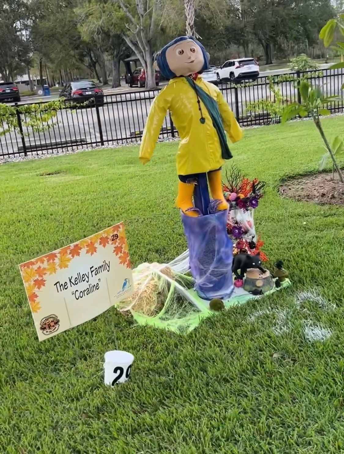 A scarecrow is standing in the grass next to a sign.