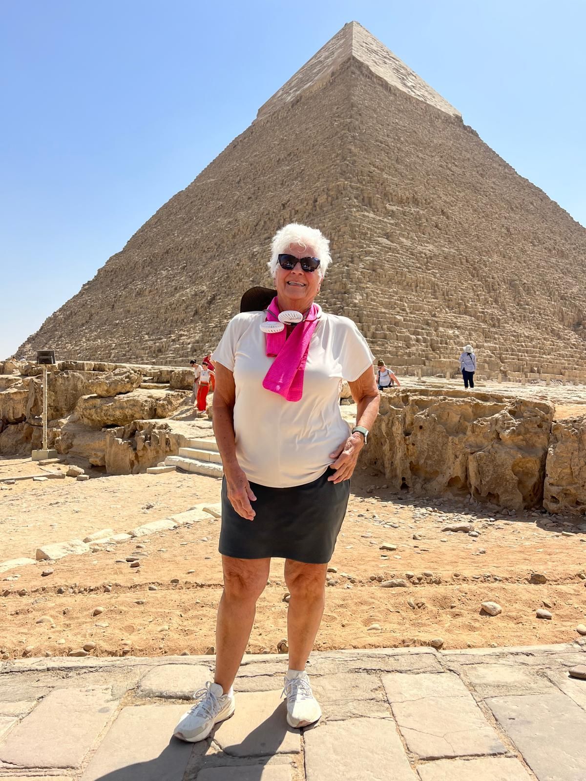 Woman in front of the Great Pyramid, Giza, Egypt; wearing a white t-shirt, gray skirt, pink scarf, and white sneakers.