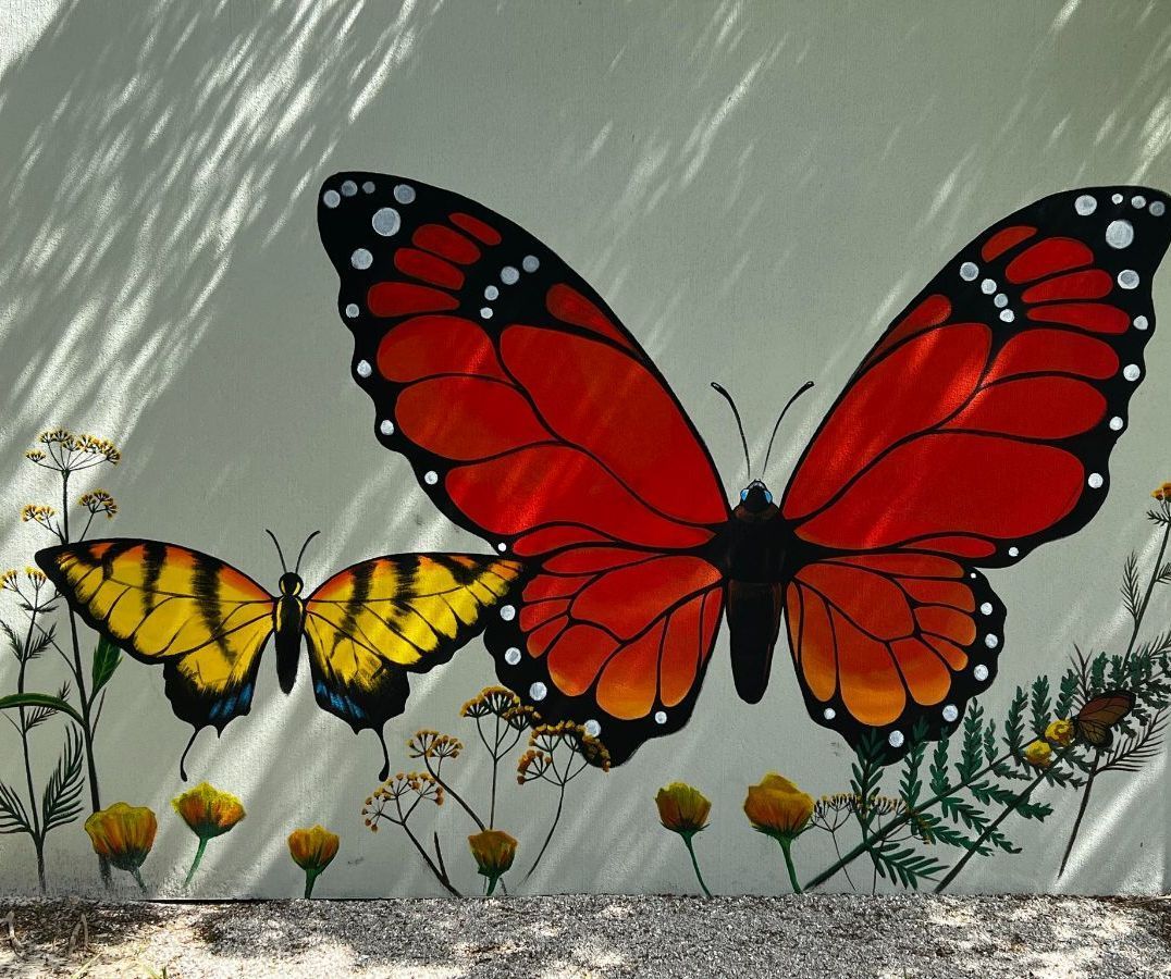 Mural of three butterflies: two yellow and black, one large red and black, with plants on a white wall.