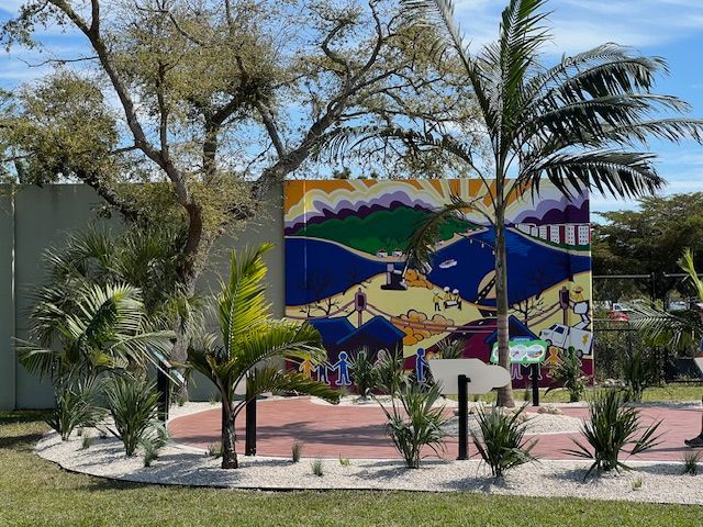 A large painting on a wall in a park surrounded by palm trees.