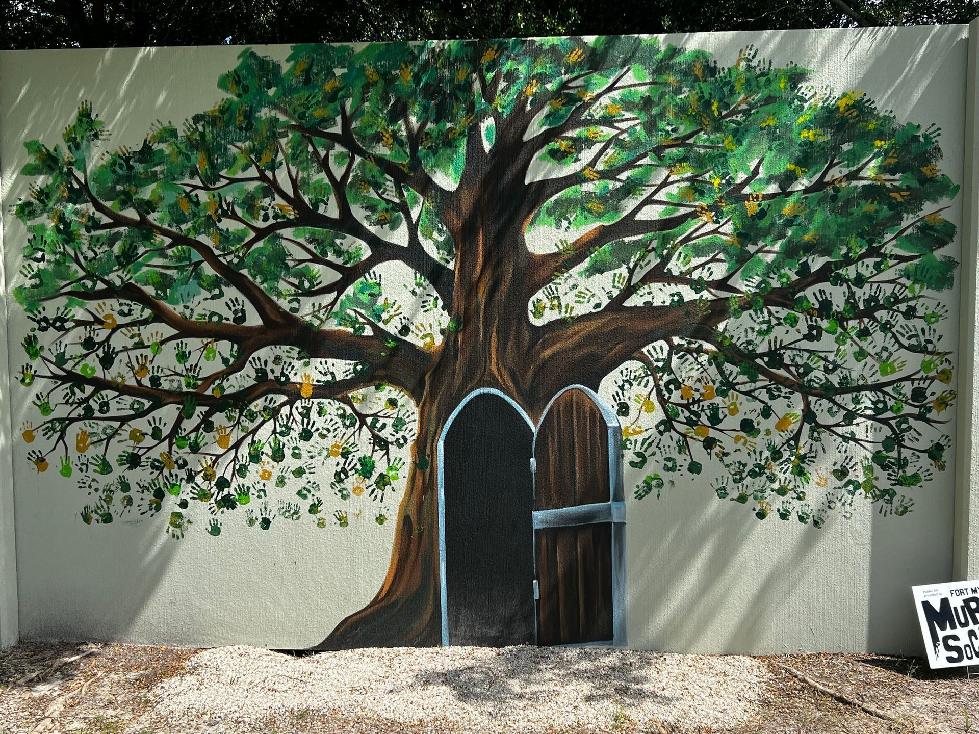 Mural: Brown tree with green leaves, door in trunk. Sunlight casts shadows.