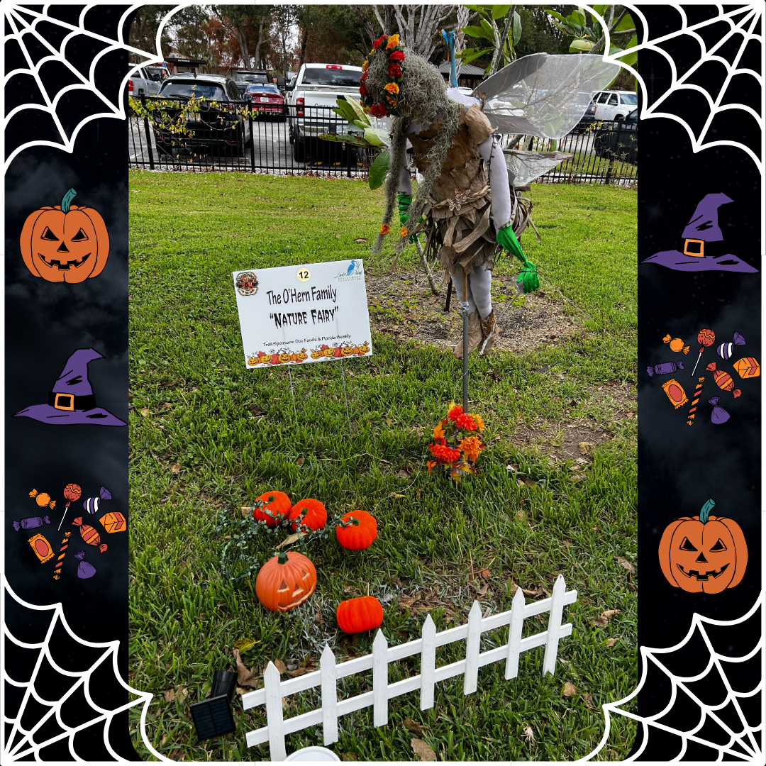 A scarecrow is sitting in the grass with pumpkins and a sign.