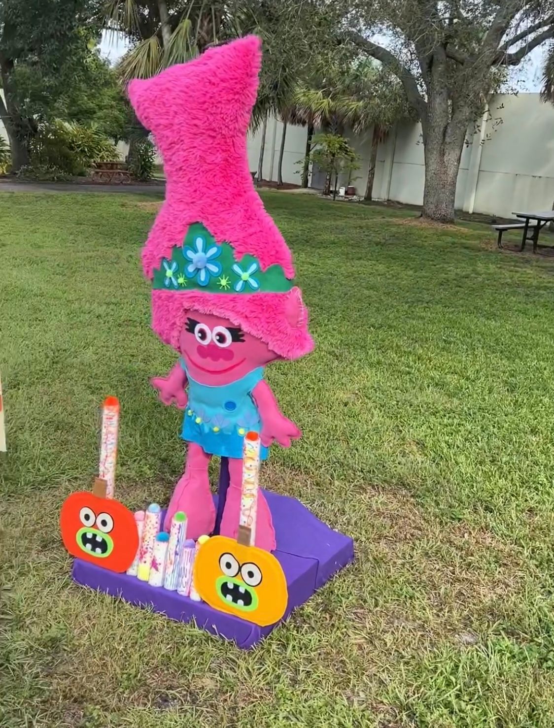A troll doll is sitting on top of a purple box in the grass.