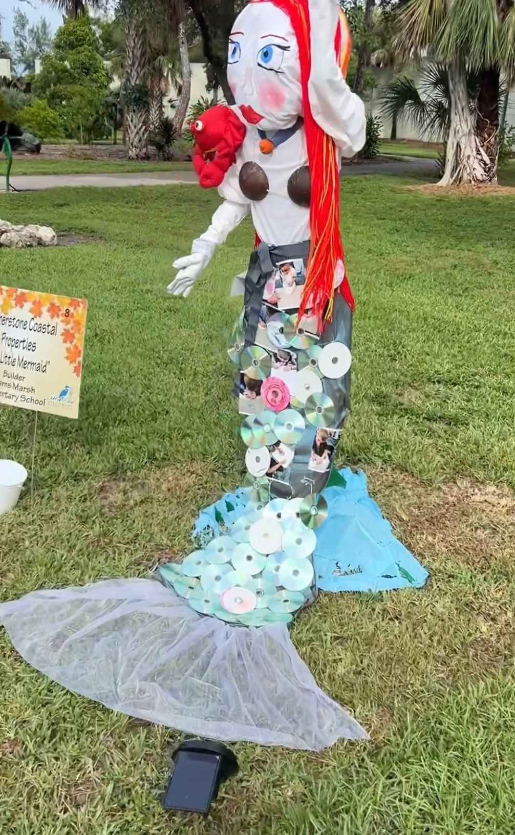 A scarecrow in the shape of a mermaid is standing in the grass.
