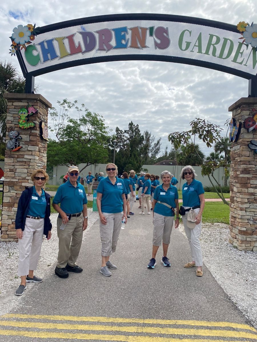 A group of people are standing in front of a children 's garden sign.