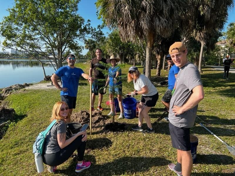 A group of people are standing around a tree in a park.