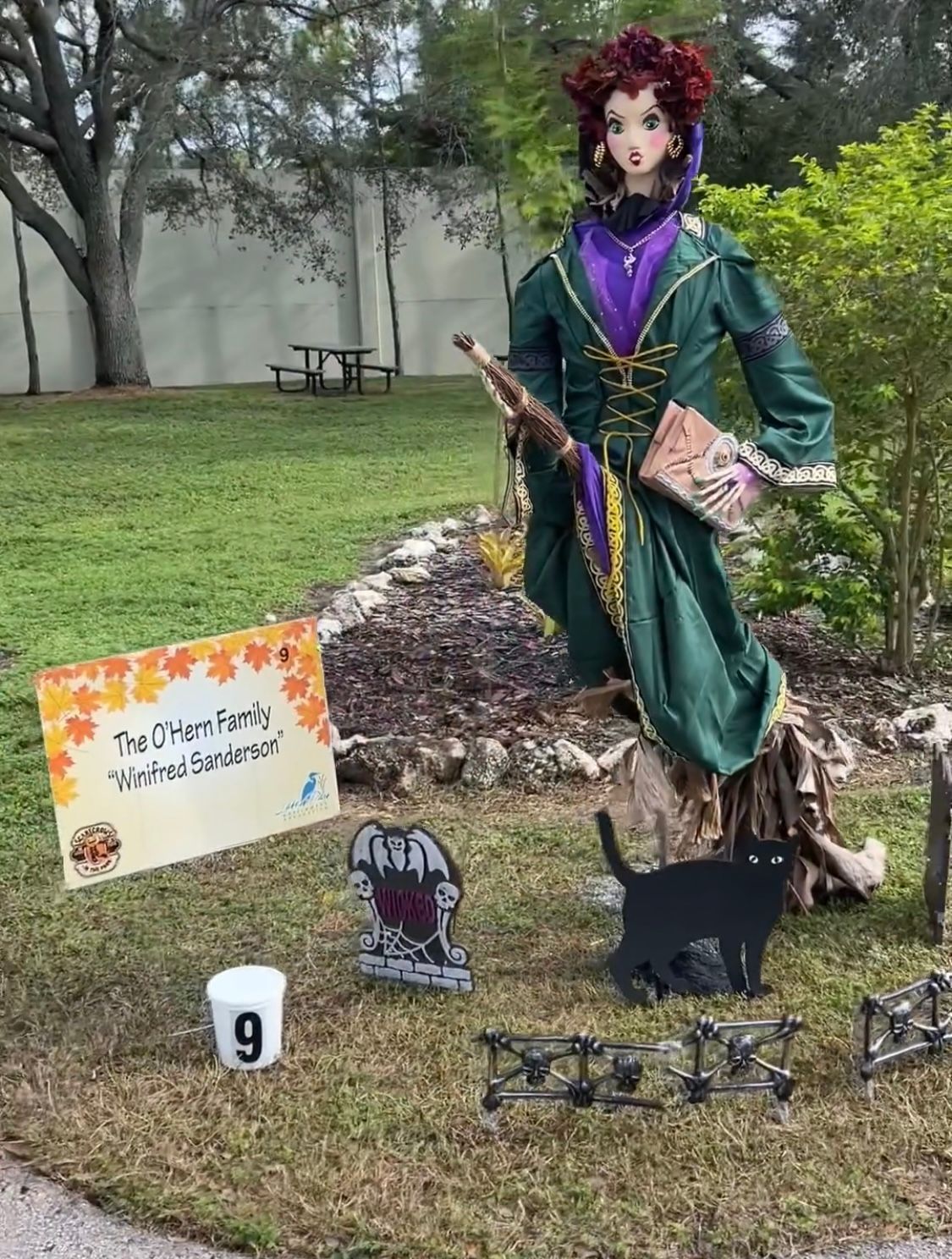 A scarecrow of a witch is sitting on a tree stump in a yard.