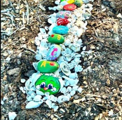 A row of rocks painted to look like a caterpillar are laying on the ground.