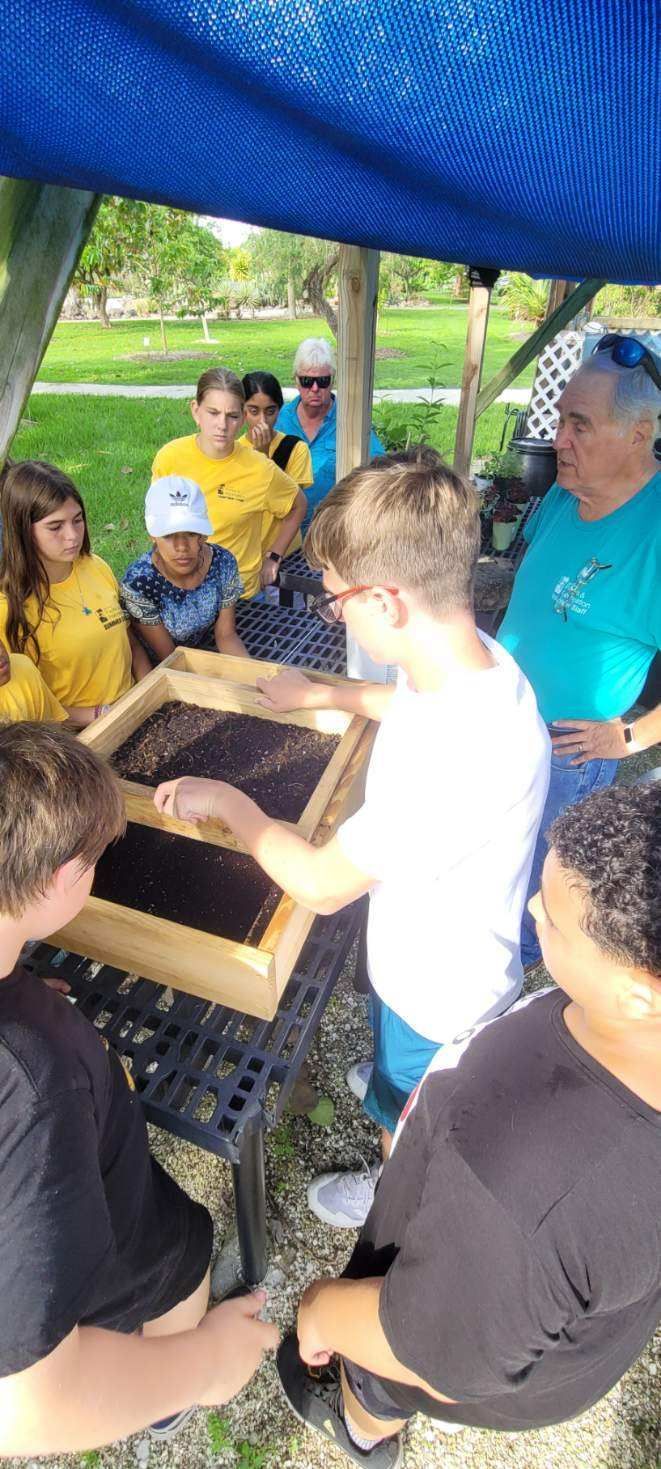 A group of people are sitting around a table looking at a beehive.