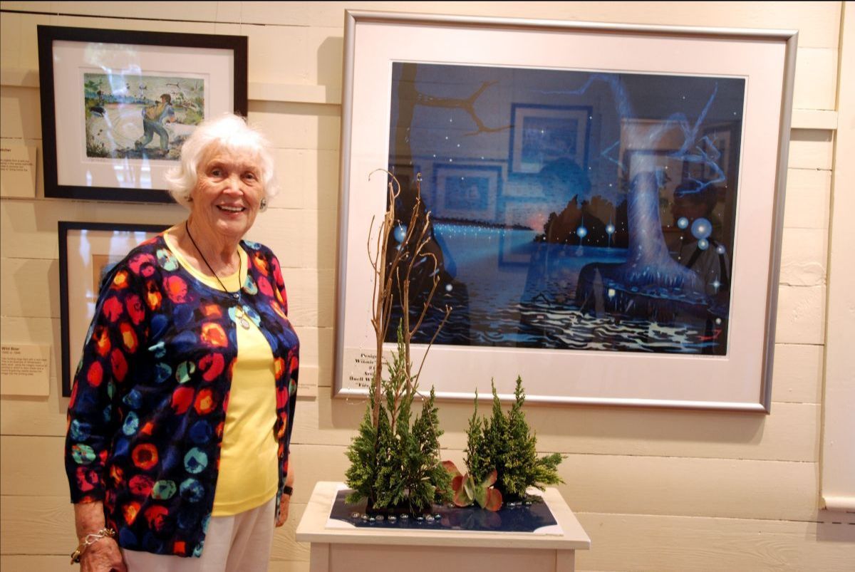 A woman is standing in front of a painting of a waterfall.