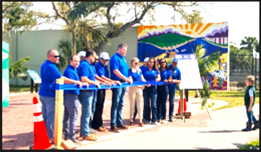 A group of people in blue shirts are cutting a blue ribbon
