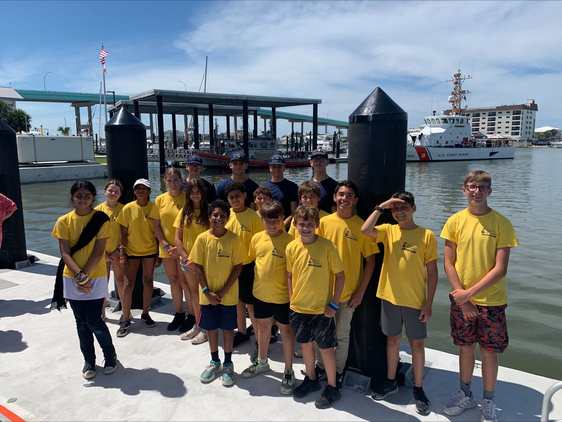 A group of young people standing on a dock next to a body of water.