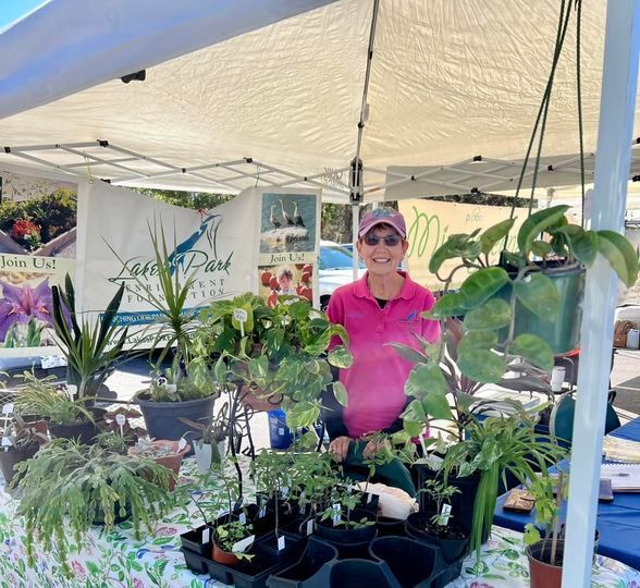 A woman in a pink shirt is standing in front of a table full of potted plants