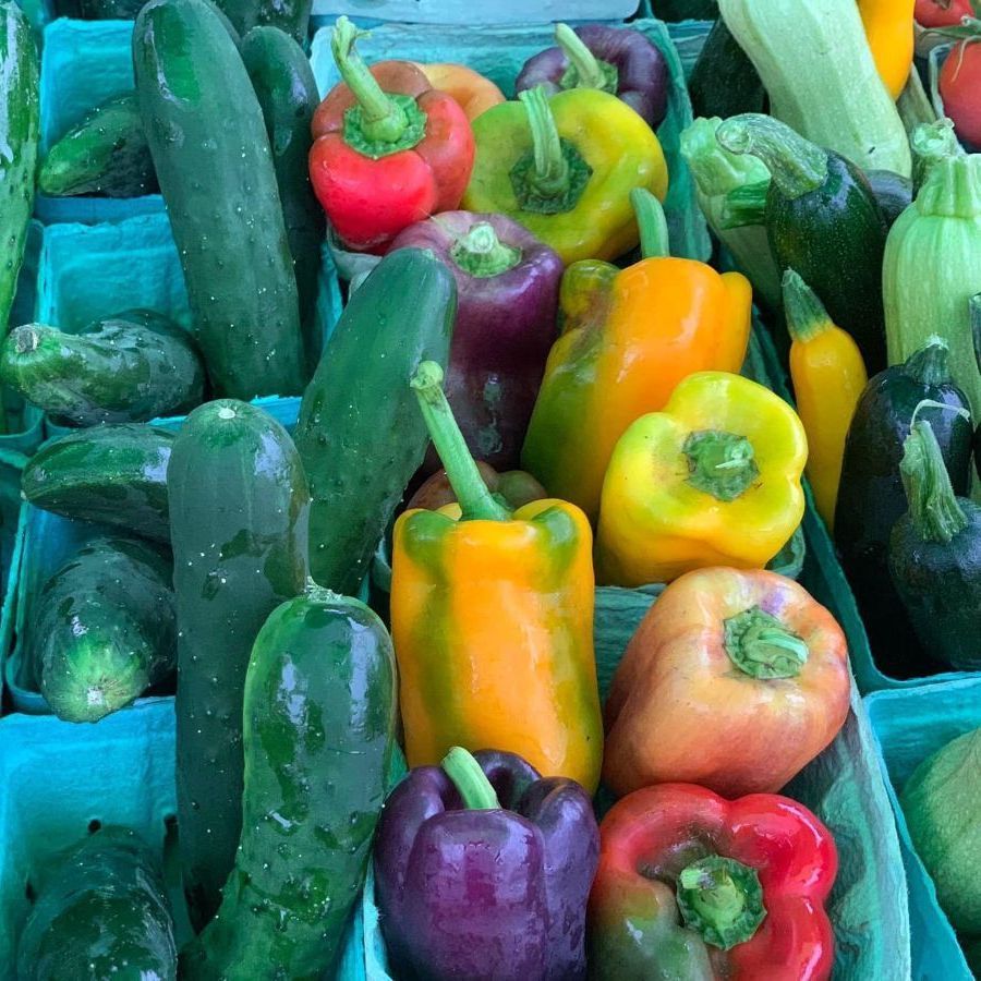 There are many different types of peppers and cucumbers in the baskets.