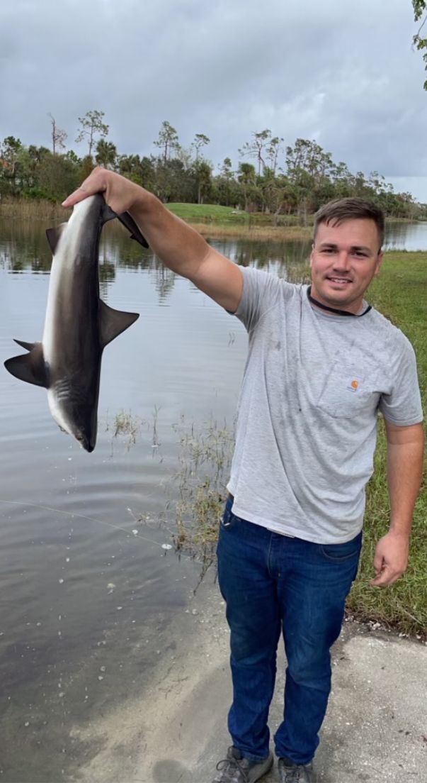 A man is holding a large shark in his hands in front of a body of water.