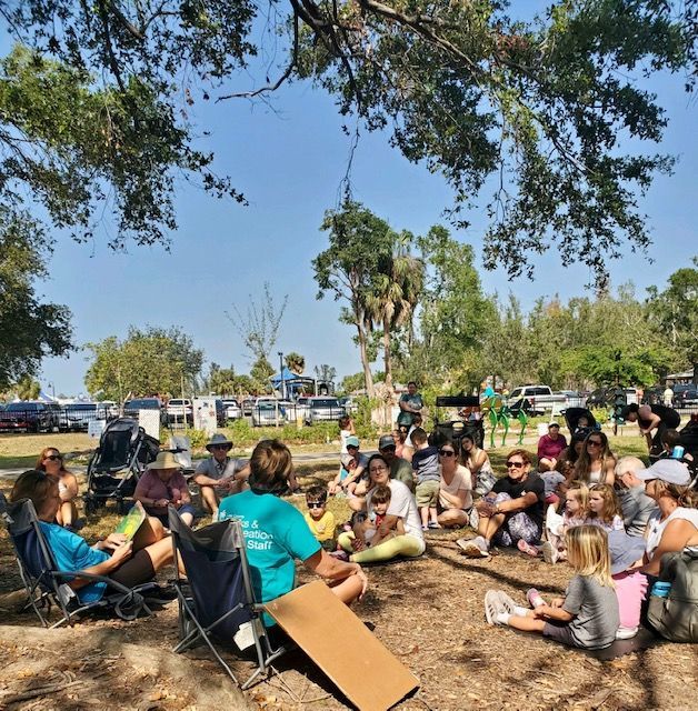 A group of people are sitting under a tree in a park