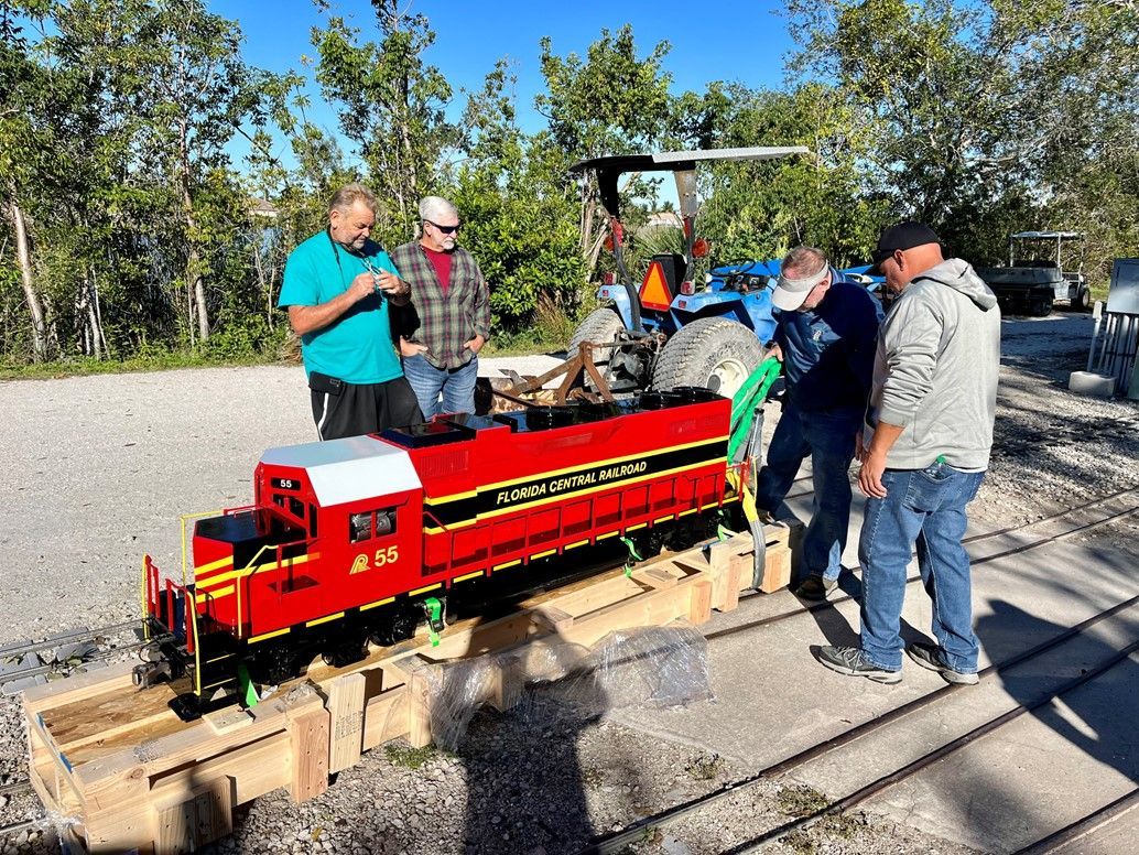 A group of men are standing around a small red train.