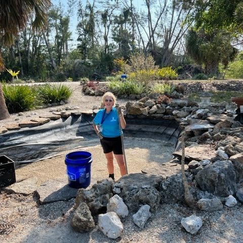 A woman is standing next to a blue bucket in a rocky area.