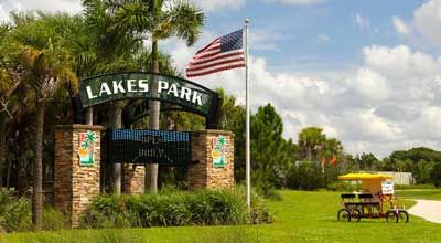 A sign for lakes park with an american flag flying in the background.