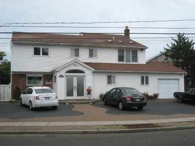 Two-story suburban house with a driveway and three parked cars under an overcast sky