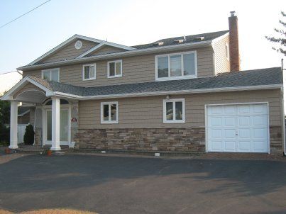 Two-story suburban house with tan siding, stone facade, white garage, and front porch