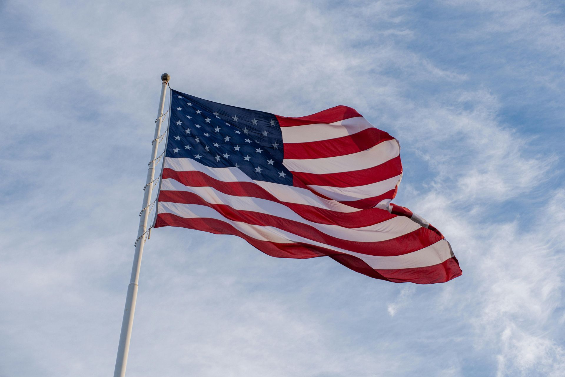 The United States flag flying on a pole against a blue, cloudy sky.