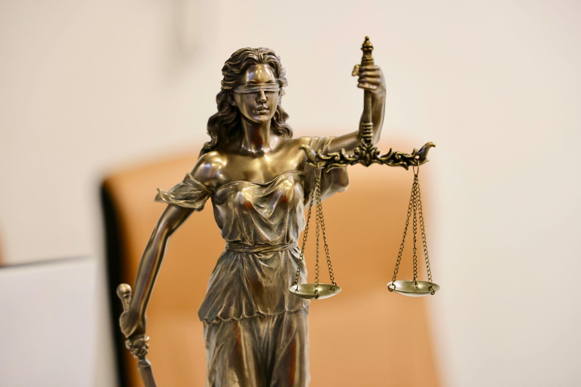 A bronze statue of Lady Justice wearing a blindfold, holding a sword in one hand and a balance scale in the other.