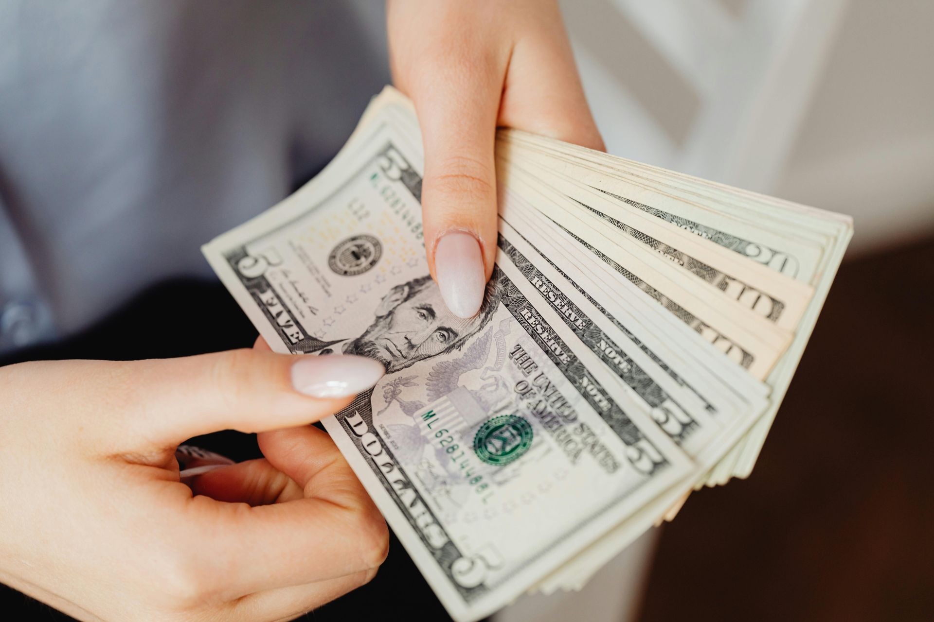 Hands holding a fan of U.S. five-dollar bills.