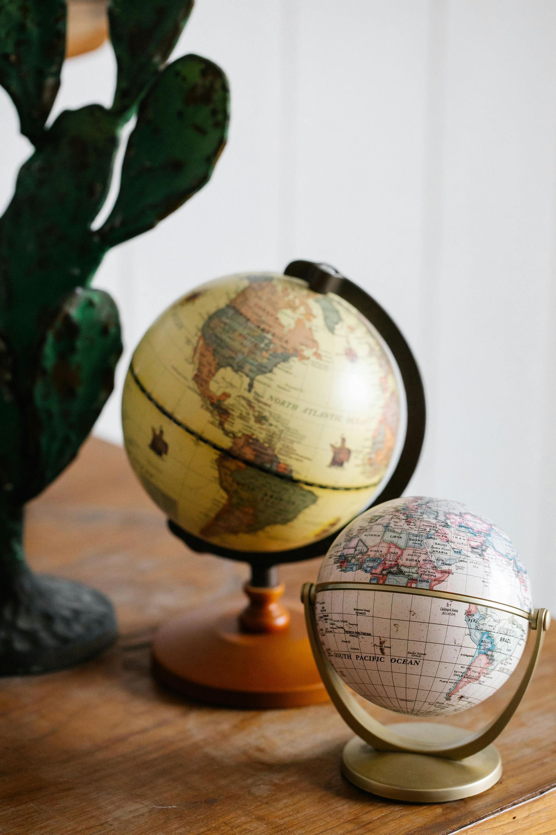 Two decorative globes on a wooden surface next to a faux green cactus.