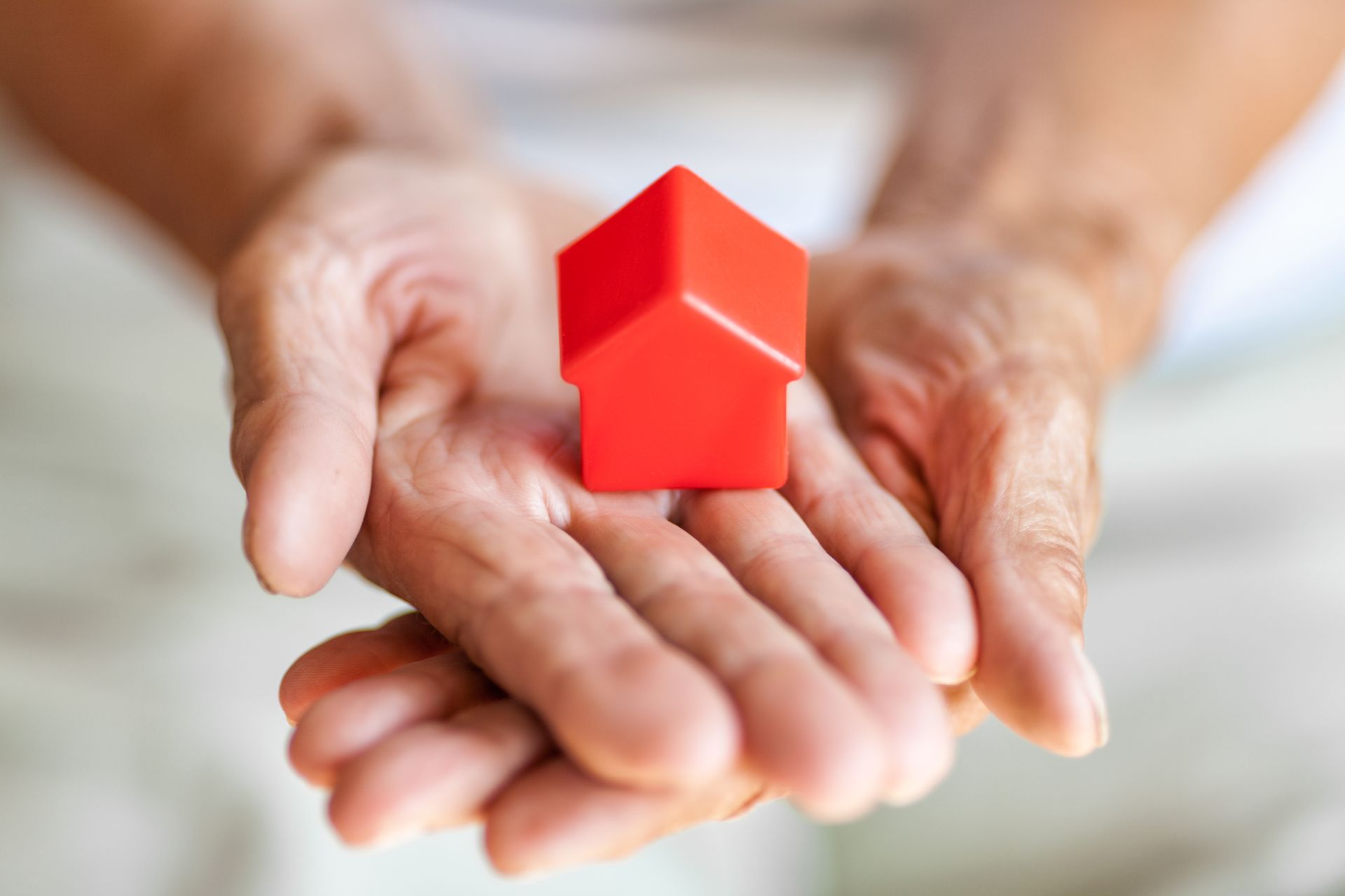 A pair of cupped hands holding a small, red, stylized house icon.