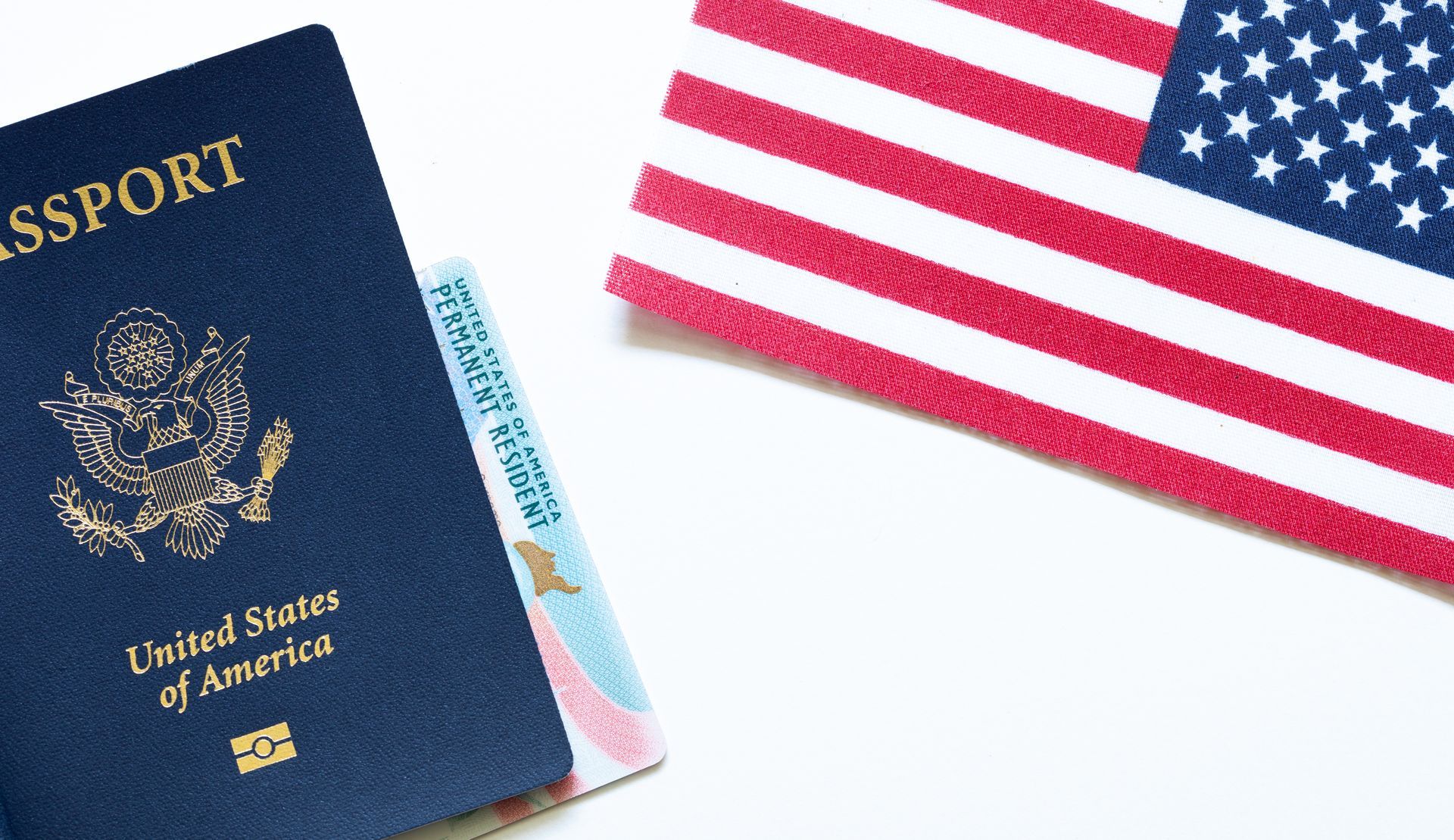 A United States passport resting next to a small, fabric American flag on a white background.