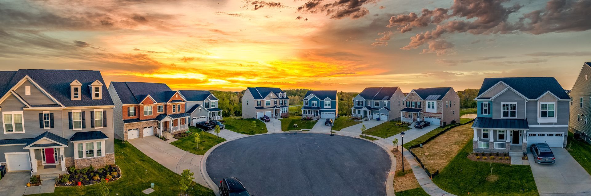 A panoramic view of a suburban cul-de-sac at sunset, featuring several large houses under a vibrant, golden sky.