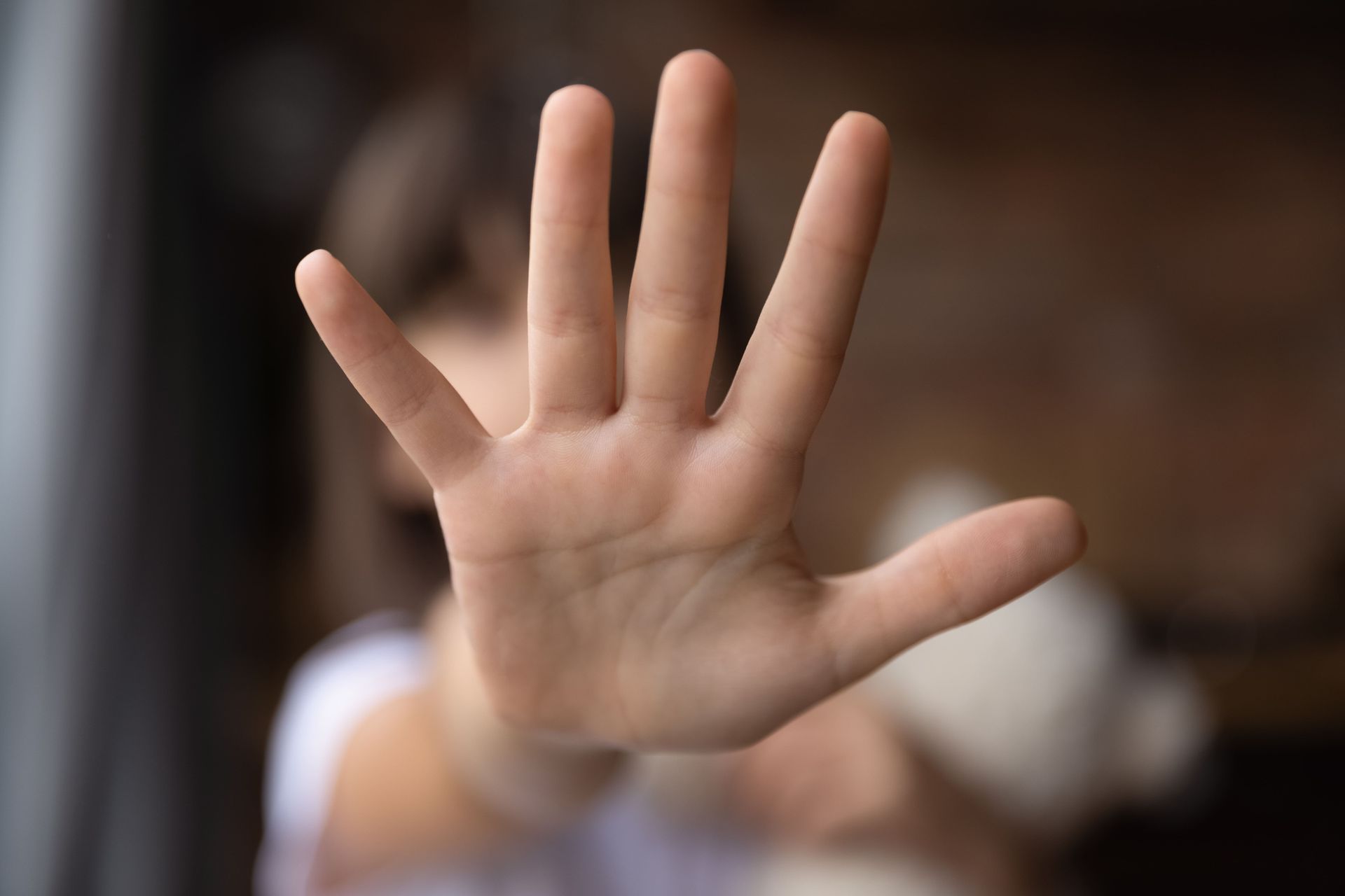 Close-up of a hand held up with palm facing forward, gesturing to stop or ward off, against a blurred background.