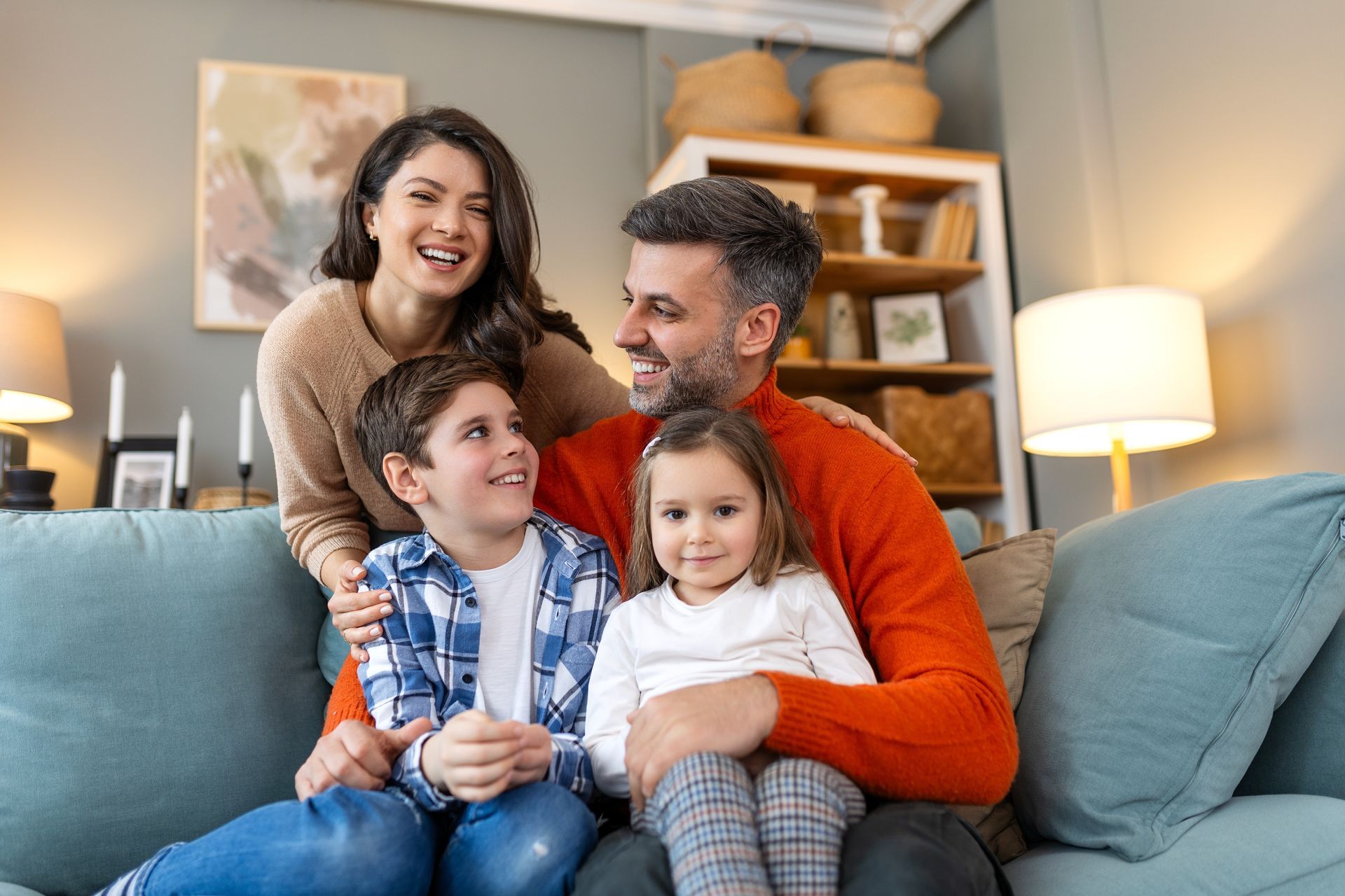 A family of four sitting on a blue sofa, smiling in a brightly lit living room.