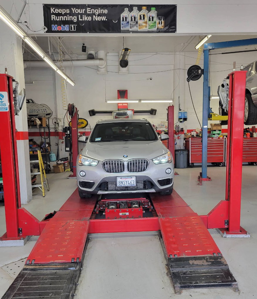 Silver BMW on a red car lift inside an auto repair shop with garage equipment and tools nearby | Chestnut Auto Repairs & Towing