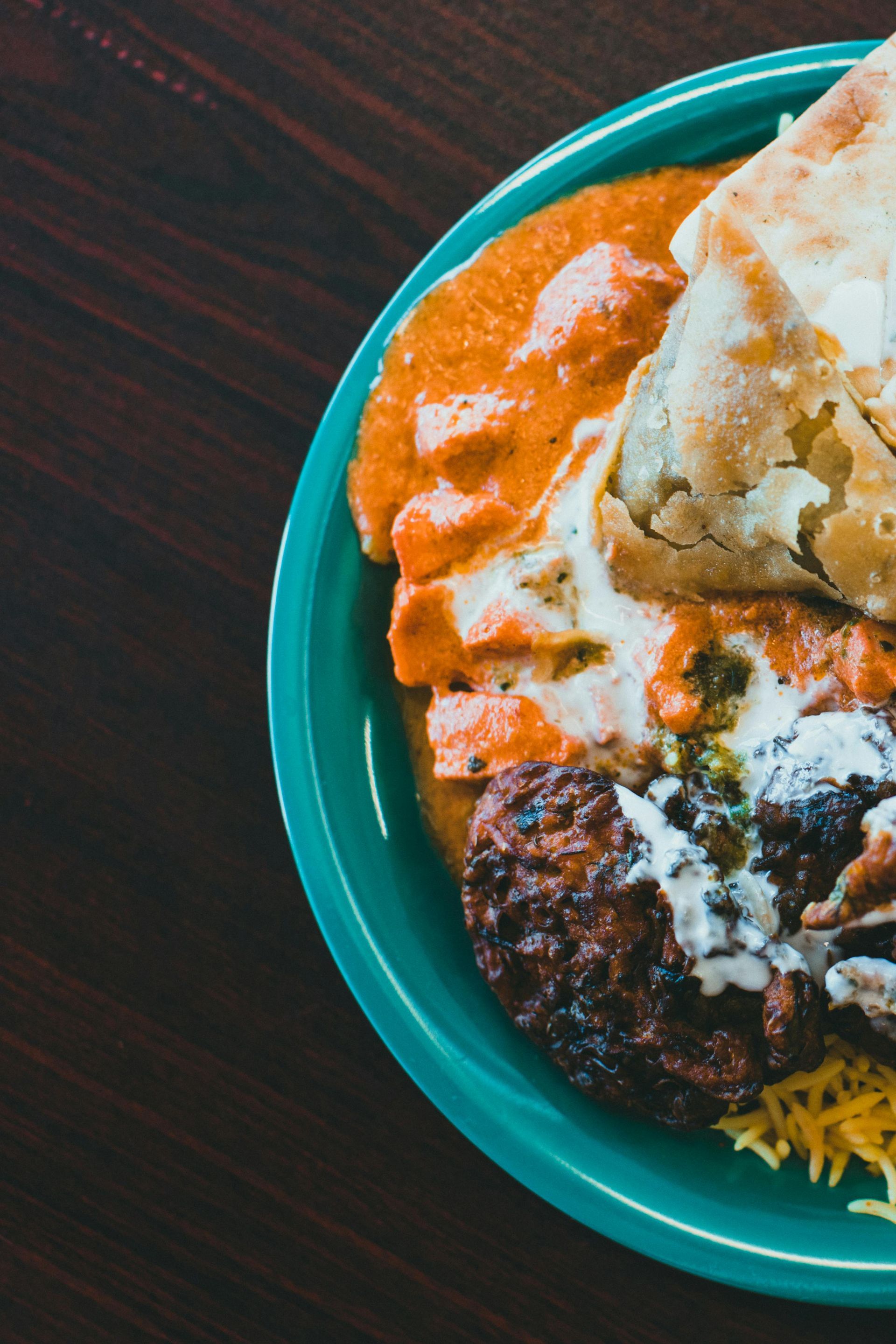 Turquoise plate with curry, rice, and naan on a dark table