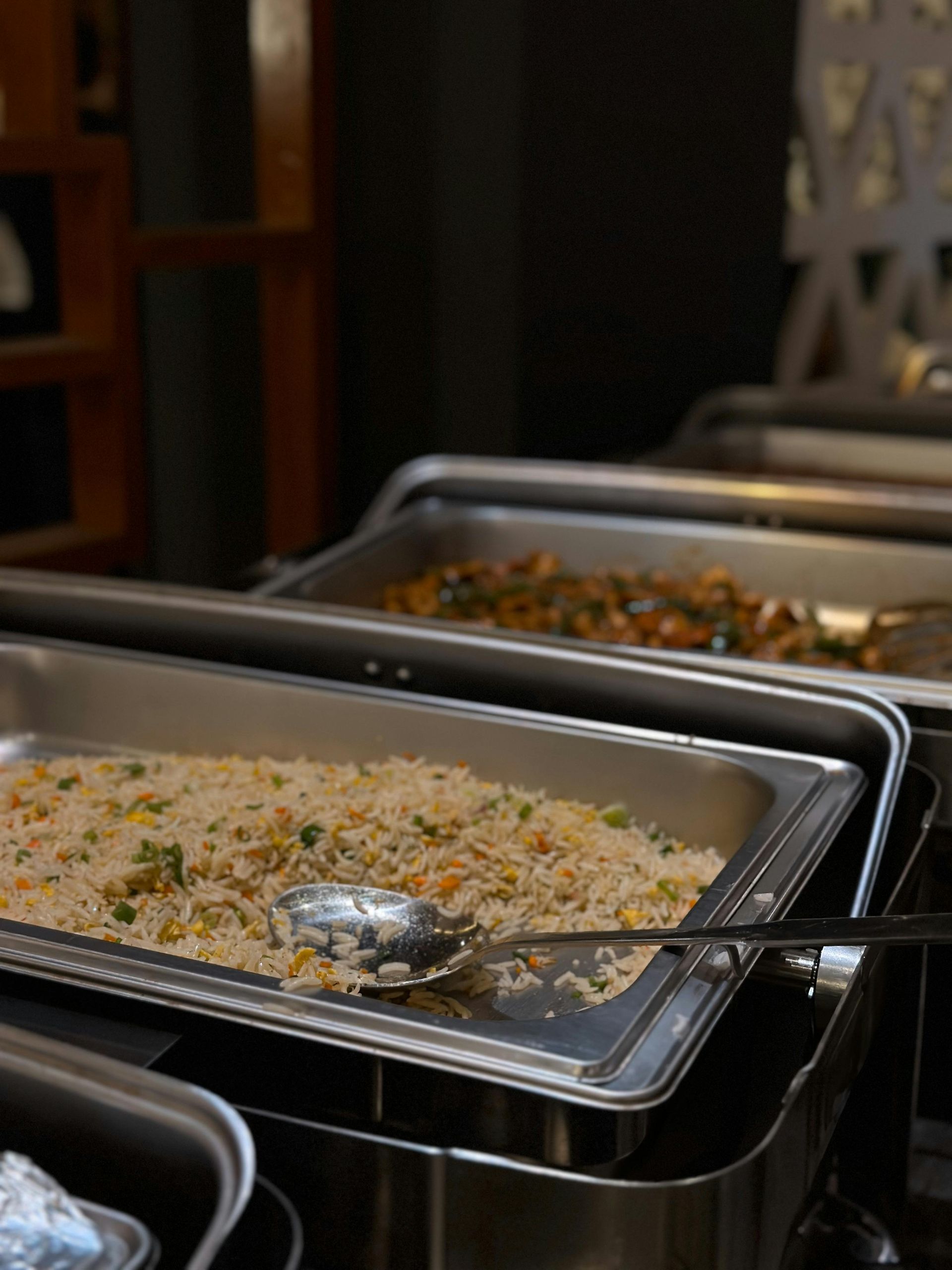 Buffet trays with rice and a serving spoon on a stainless steel counter