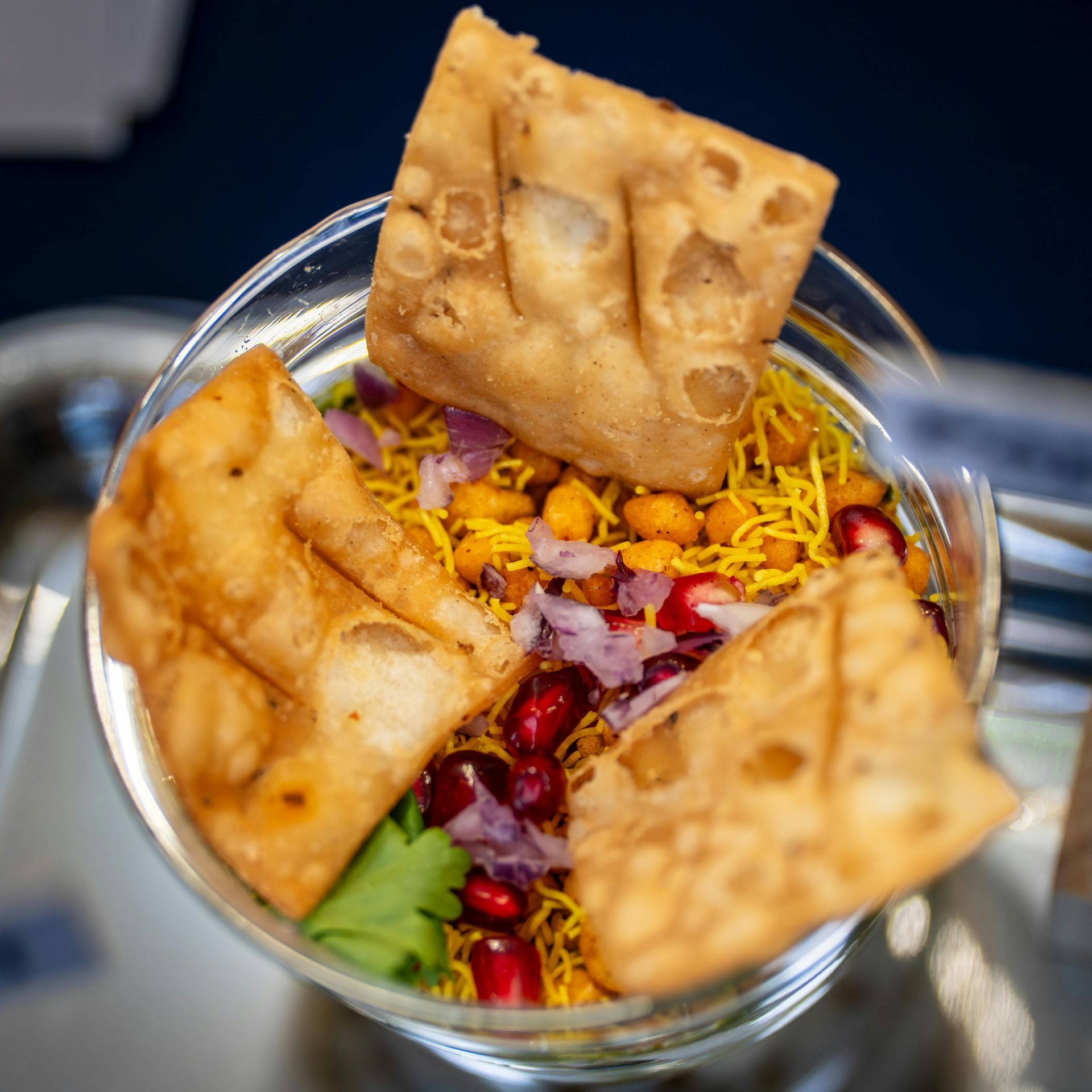 Glass bowl with colorful snack mix topped with crisp squares and pomegranate seeds