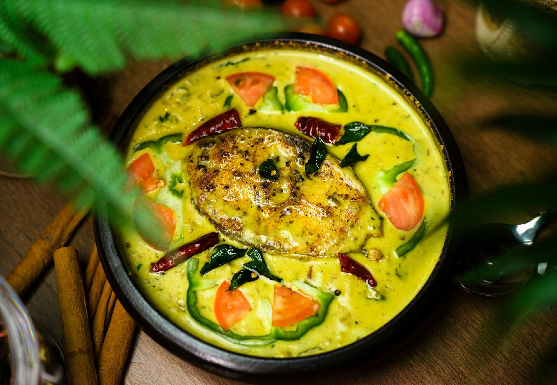Colorful curry bowl with fish, tomatoes, herbs, and dried chilies on a wooden table